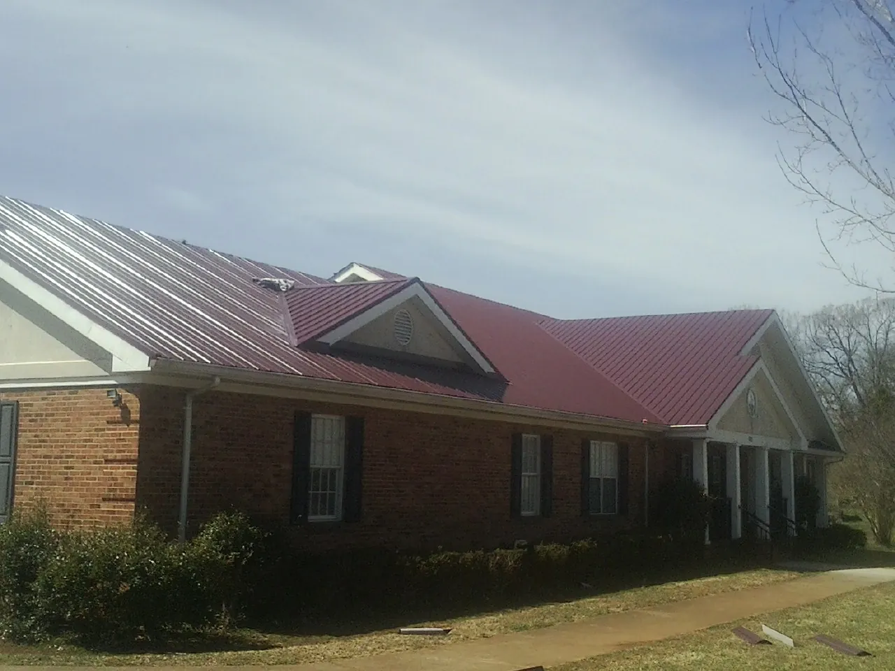 Red metal roof with gabled entries on a long brick building, from a Hail Damage Roof Repair job in Green Mountain Falls