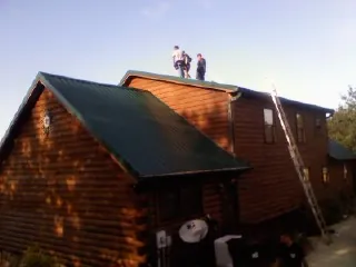 Crew on the ridge of a green metal roof on a two story log home in Green Mountain Falls