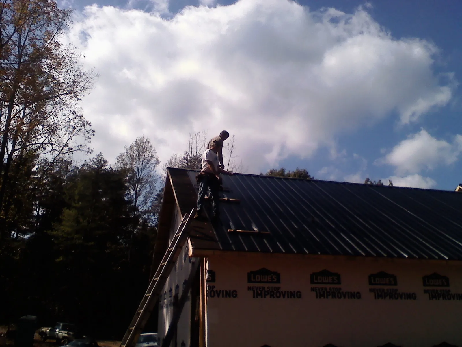 Roofer fastening dark metal panels high against a cloudy sky, from a Roof Inspection job in Green Mountain Falls