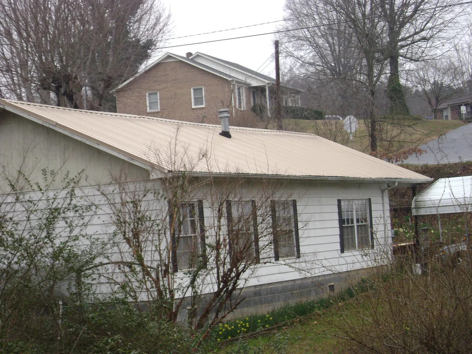 Tan metal roof on a white sided house set into a hillside — Commercial Roofing by Roofing Brothers in Green Mountain Falls